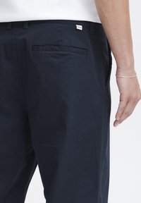 Granatowe spodnie bawełniane, z płaską tylną kieszenią i metką marki. Gładka tekstura z prostym krojem.