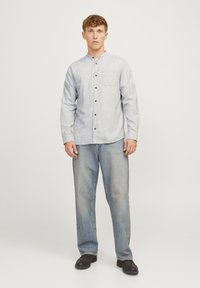 Heledad sinine nööbiga särk, millel on krae ja rinna tasku, pruuni nööbiga, koos lõdva istuvusega heleda sinise teksapükse ja mustade kingadega.