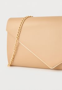 Pochette enveloppe beige avec une chaîne dorée et un détail de bordure métallique sur le rabat, posée sur un fond blanc.