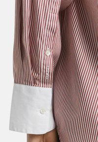 Rot-weißer gestreifter Langarmshirt, mit weißen Manschetten, Knopfdetail und gesticktem Markenlogo auf dem Ärmel.
