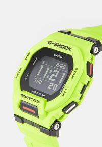 Montre numérique G-SHOCK avec un boîtier et un bracelet en résine de couleur verte vif, accents noirs, grand affichage montrant l'heure, la date et des fonctionnalités étiquetées sur la lunette.