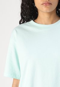 Jasnoturkusowa bawełniana koszulka z okrągłym dekoltem i krótkimi rękawami, charakteryzująca się gładką fakturą i luźnym krojem.