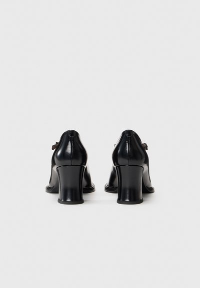 Escarpins en cuir verni noir avec des talons carrés, des arrières arrondis et une finition lisse et brillante. Présente un accent de boucle décorative.
