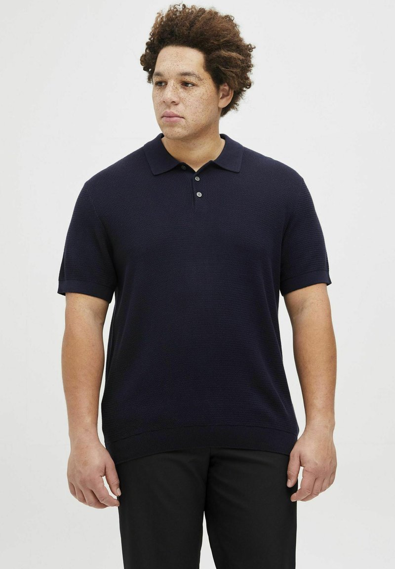 Tamsiai mėlynas trumpų rankovių polo marškinėliai su tekstūriniu raštu, trijų mygtukų apykakle ir gumas apykakle. Suderinta su tamsiomis kelnėmis.