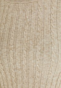 Pull en maille beige clair présentant une texture à côtes verticales avec des motifs en tricot à torsades partout. Tissu doux avec une finition lisse.
