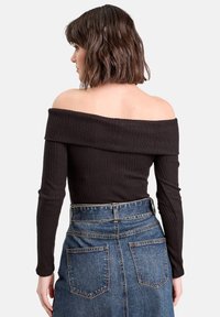 Donna con capelli corti castani che indossa un top a costine nero off-the-shoulder e una gonna di jeans blu a vita alta, vista di spalle.