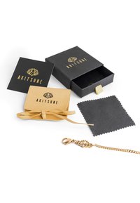 Gold-colored chain with a lotus clasp, a tan felt pouch, a dark cleaning cloth, and a black box with gold logo details.
