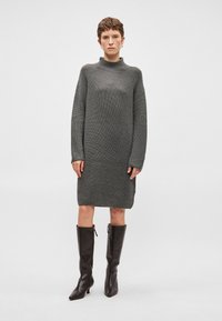 Abito lavorato a maglia grigio con collo alto e maniche lunghe, che arriva a metà coscia. Abbinato a stivali di pelle marrone al ginocchio.