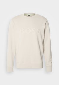 Ljus beige sweatshirt i mjukt tyg, med rund halsringning och långa ärmar. Ordet "BOSS" är tydligt präglat framtill.