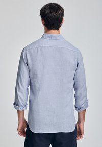 Jasnoniebieska lniana koszula z podwiniętymi rękawami, zapinana na guziki, z prostym wykończeniem pleców, prezentująca teksturowany, oddychający materiał.