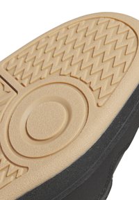 Skosula med en strukturerad, ljusbeige gummiyta som har cirkulära och zigzag-mönster, kantad med svart syntetmaterial.