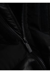 Acercamiento a una cremallera negra con un tirador de metal en una chaqueta acolchada, mostrando las costuras detalladas y la textura de la tela.