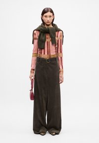 Haut à manches longues, à motifs en rose et beige, écharpe vert olive, pantalon large marron foncé et petit sac à main rouge avec une longue bandoulière.