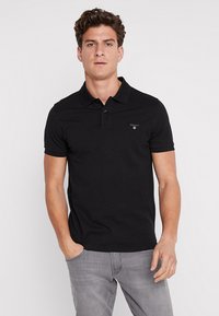 Sort bomulds polo shirt med krave, tre knapper og broderet logo på venstre side. Korte ærmer og en tætsiddende pasform.