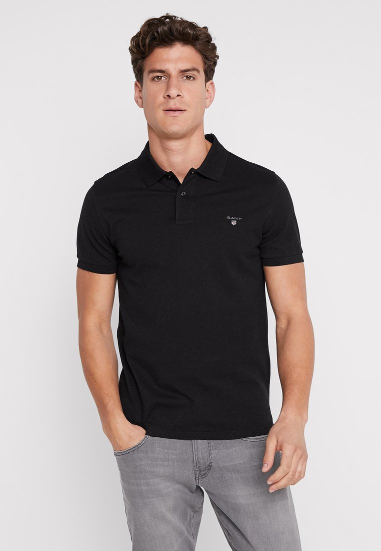 Sort bomulds polo shirt med krave, tre knapper og broderet logo på venstre side. Korte ærmer og en tætsiddende pasform.