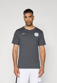 T-shirt grigia a maniche corte realizzata in tessuto morbido, con collo rotondo, logo Nike in bianco ed emblema di Parigi sul lato sinistro del petto.