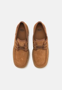 Paire de chaussures mocassin en daim marron avec des lacets assortis et des semelles cousues, vue de dessus sur un fond neutre.