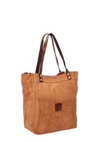 Beige suède draagtas met bruine leren handvatten, voorzien van een vierkante logovlek en zilverkleurige metalen details. Zachte textuur, rechthoekige vorm.