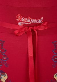 Punainen vaate, jossa on kukkakuvioita, ja jossa on brodeerattu "Desigual" -logo sekä satiininen nauha vyötäröllä. Täydellisen sileä kankaan rakenne.