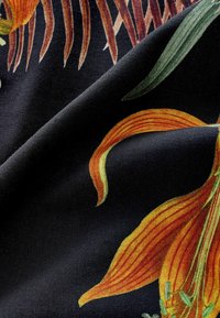 Virágmintás textil, narancssárga és zöld liliom mintákkal, fekete háttéren. Simány tapintású, élénk színekkel és részletes mintákkal.