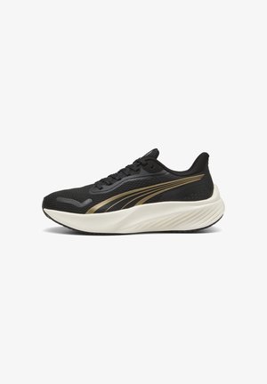 Chaussure de sport noire avec bandes latérales dorées et semelle blanche épaisse, munie d'une tige en mesh et d'un design à lacets, vue de côté sur fond blanc.
