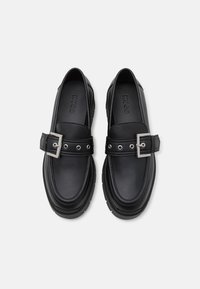 Mocassins en cuir noir avec une boucle carrée, une quincaillerie en argent et une couture décorative. Design de semelle légèrement surélevée et épaisse.