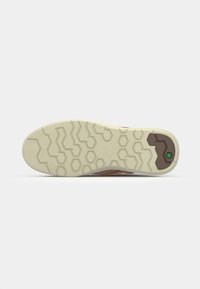 Vista de la suela del zapato que presenta una suela de goma beige con un patrón hexagonal y un acento marrón en el talón, proporcionando agarre y soporte.