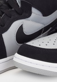 Gros plan sur des baskets Nike noires et grises montrant des lacets texturés, le logo swoosh cousu, un embout perforé et des détails de la semelle en caoutchouc.