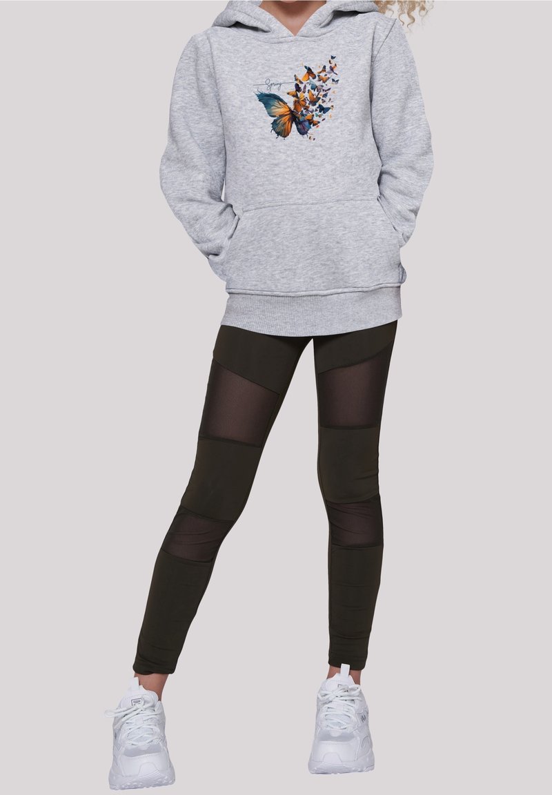 Felpa grigia con grafica di farfalla, dotata di tasca frontale. Leggings neri con pannelli in rete, finitura texturizzata, abbinati a sneakers bianche.