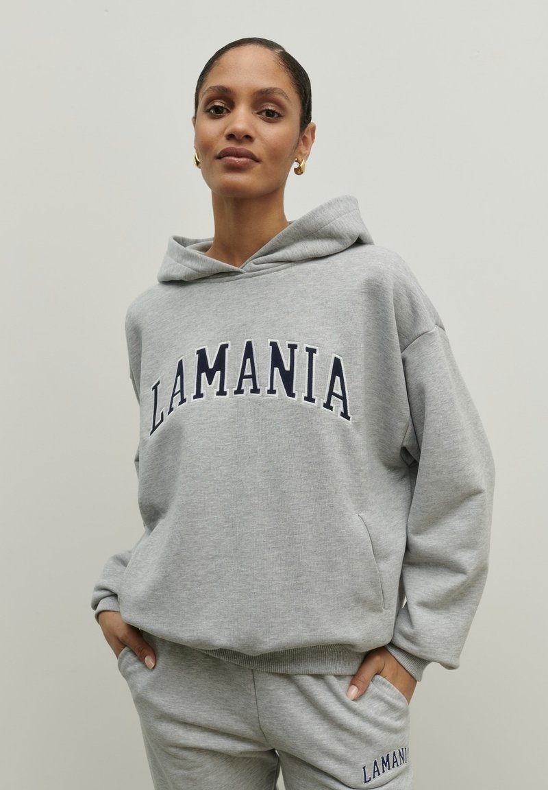 Šedá mikina vyrobená z měkké látky, s přední kapsou a nápisem "LAMANIA" ve tmavě modrých písmenech přes hruď. Každodenní, volný střih.
