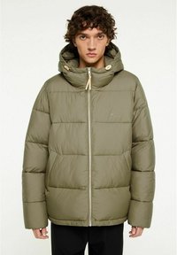 Vadderad olivgrön jacka med huva, framdragkedja och togglar. Har en quiltad design och lös passform, lämplig för kallt väder.