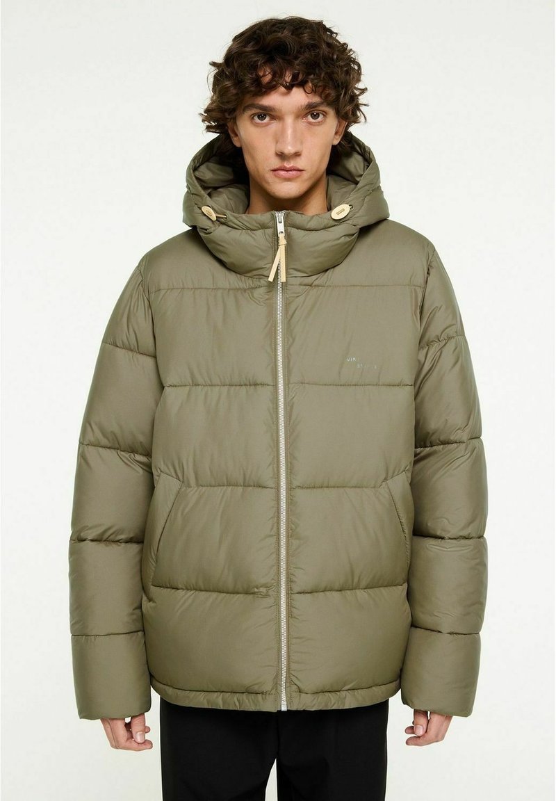 Vadderad olivgrön jacka med huva, framdragkedja och togglar. Har en quiltad design och lös passform, lämplig för kallt väder.