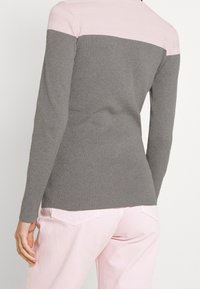 Henkilö, jolla on päällään harmaa ja vaaleanpunainen ribatattu pitkähihainen villapaita, yhdistettynä vaaleanpunaisiin housuihin, näkyy takaa vyötäröstä alaspäin.