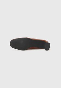 Chaussure habillée en cuir marron vue de la semelle, présentant une semelle extérieure en caoutchouc noir texturé et un petit talon rectangulaire.