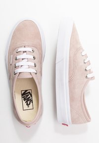 Sneakers Vans in suede rosa chiaro con lacci e suole bianche, uno mostrato dall'alto e l'altro di lato, su sfondo bianco.