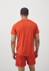 Miesten urheiluasu, joka sisältää lyhythihaisen kirkkaan oranssin paidan ja kuvioidut oranssit shortsit, molemmat kevyttä kangasta.