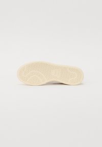 Hvide sneakers med en struktureret gummisål, der har et hexagonalt mønster. Hælen viser en let indrykning, hvilket indikerer et afslappet design.