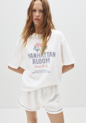 T-shirt blanc en coton avec un col rond et des manches courtes, orné d'une broderie florale, du texte "Manhattan Bloom" et d'un short à coupe décontractée.