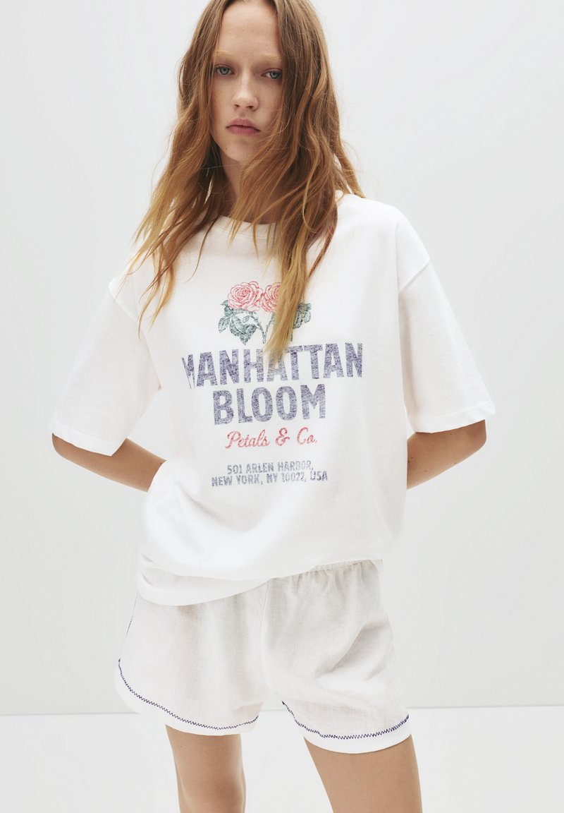 Bílá bavlněná tričko s kulatým výstřihem a krátkými rukávy, zdobené květinovou výšivkou, s nápisem "Manhattan Bloom" a volnými šortkami.
