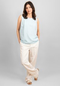 Haut sans manches bleu clair en tissu doux, associé à un pantalon en lin écru. La tenue présente une coupe décontractée et un style informel.