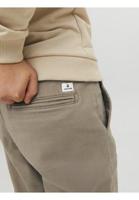 Beige sweatshirt och ljusgrå byxor, med en synlig etikett på bakfickan, ribbade muddar och textil med struktur.