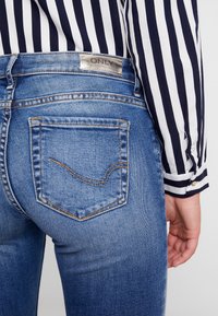 Blå denimjeans med en åtsittande design, med en silveretikett på baksidan och två bakfickor med orange sömdetalj.
