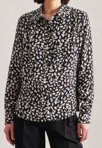 Camicia button-up nera e crema con un motivo di forme astratte, maniche lunghe e colletto a punta. Tessuto leggero con una texture liscia.