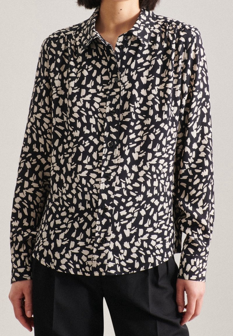 Camicia button-up nera e crema con un motivo di forme astratte, maniche lunghe e colletto a punta. Tessuto leggero con una texture liscia.