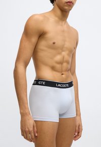 Boxer aderenti azzurri con una fascia elastica nera con il logo "LACOSTE". Il design è aderente con una texture liscia e lunghezza fino a metà coscia.