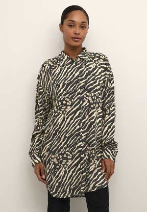 Chemise à boutons en imprimé animal noir et crème. Dotée d'un col évasé, de manches longues et d'une coupe décontractée avec un ourlet légèrement courbé.