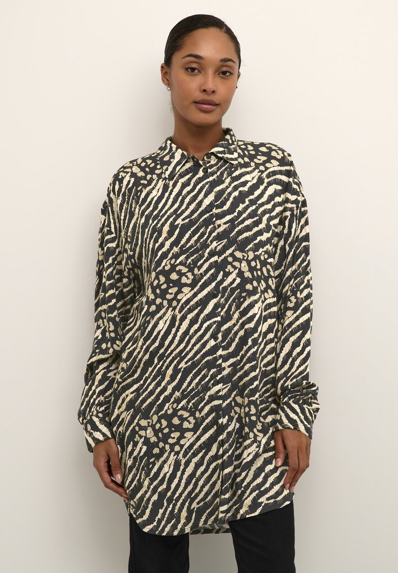 Knapbluse i sort og cremet dyreprint. Har en spread collar, lange ærmer og en afslappet pasform med en let bølget kant.