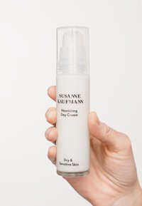 Bouteille cylindrique blanche de crème de jour nourrissante Susanne Kaufmann, dotée d'un couvercle à pompe transparent, étiquetée pour les peaux sèches et sensibles.