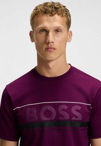 Lila kortärmad T-shirt i bomull, med en djärv "BOSS"-logotyp, horisontella ränder i svart och vitt, rund halsringning.