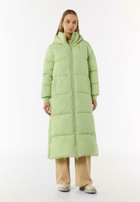 Padded long coat in light green, featuring a hood, front zipper, and snap buttons. Smooth texture with a straight cut and side pockets.